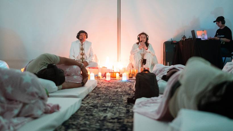 Participantes recostadas durante un baño de sonido, con dos facilitadoras al fondo entre velas